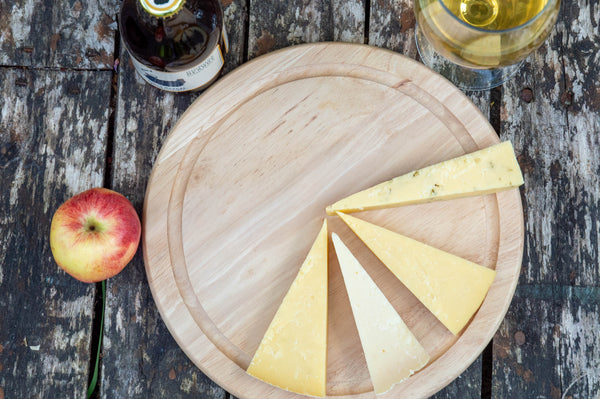 Wooden board with sliced cheese and an apple on a rustic wooden table.