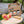 Three beer bottles in a cardboard carrier with apples and a wooden mallet on a rustic wooden table outdoors.